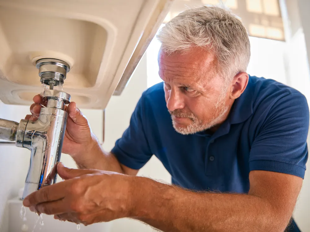 Plumber checking the drain and supply lines under a sink for leaks